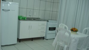 A small, clean kitchen with white cabinets, a refrigerator, an oven, and a dining table with white chairs. - Residencial Floripamar I (Florianópolis)