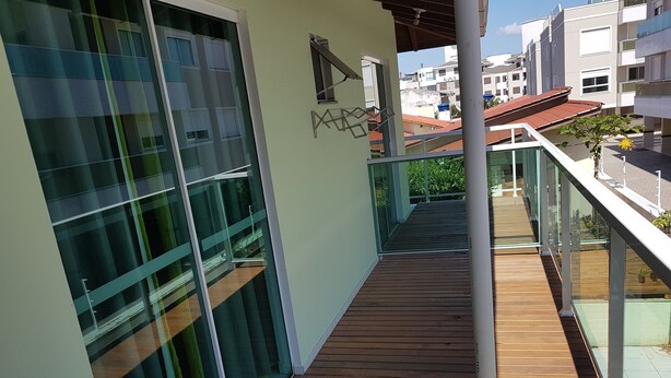 A modern balcony with glass railings, wooden flooring, and a view of neighboring buildings. - Residencial Floripamar I (Florianópolis)