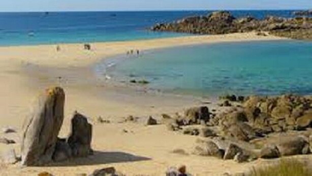 A beach with clear blue water, sandy shore, and rocky outcrops.