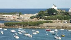 A coastal town with boats in the water, a prominent white building, and a rocky shoreline.