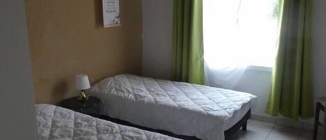 A room with two beds, a small table, a red rug, and a window with green curtains.