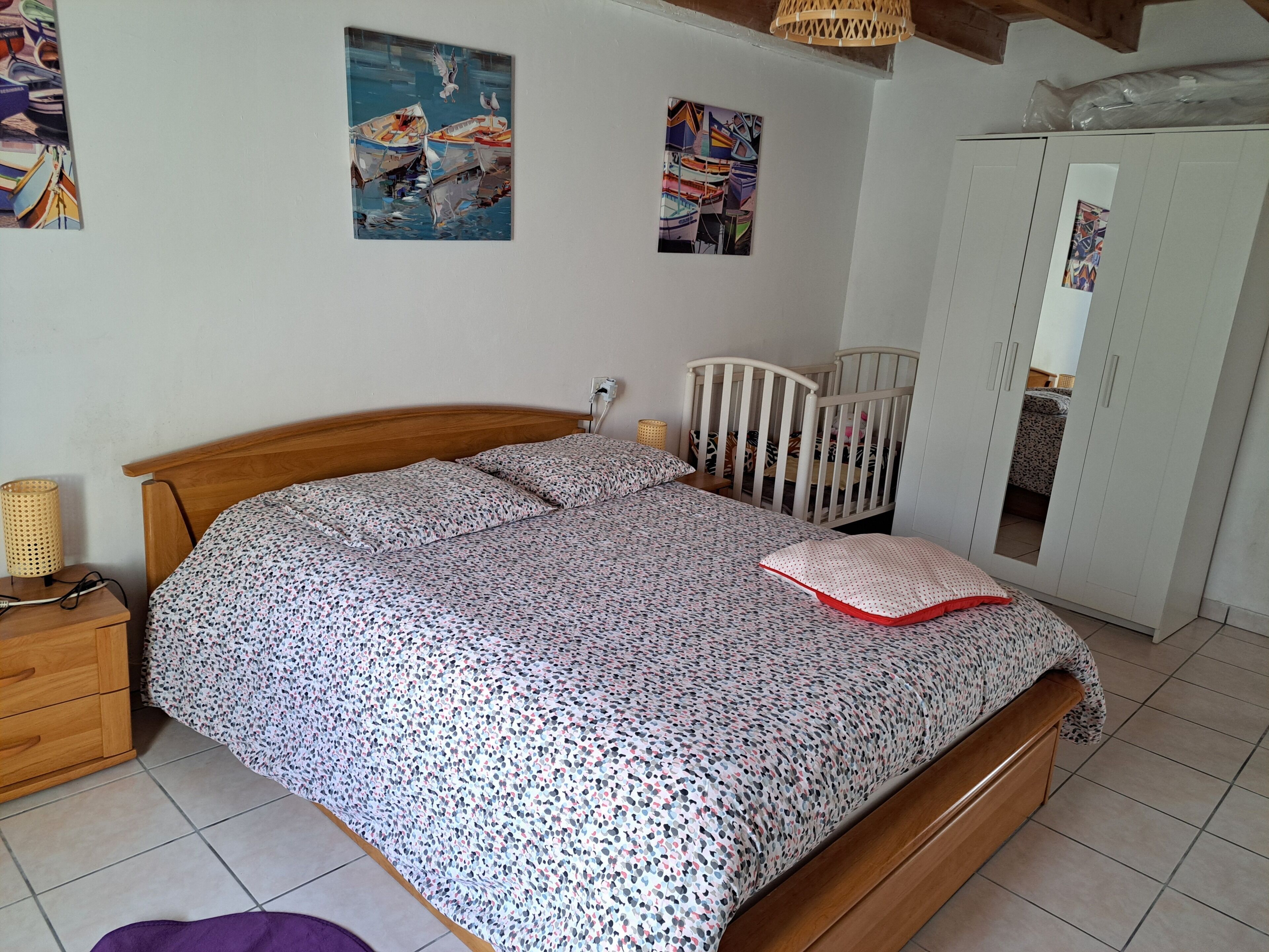 A bedroom with a wooden bed, a crib, a wardrobe, and wall art.