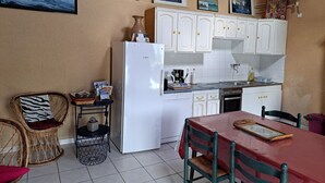 A compact kitchen with white cabinets, a Bosch refrigerator, a dining table with chairs, and a wicker chair.