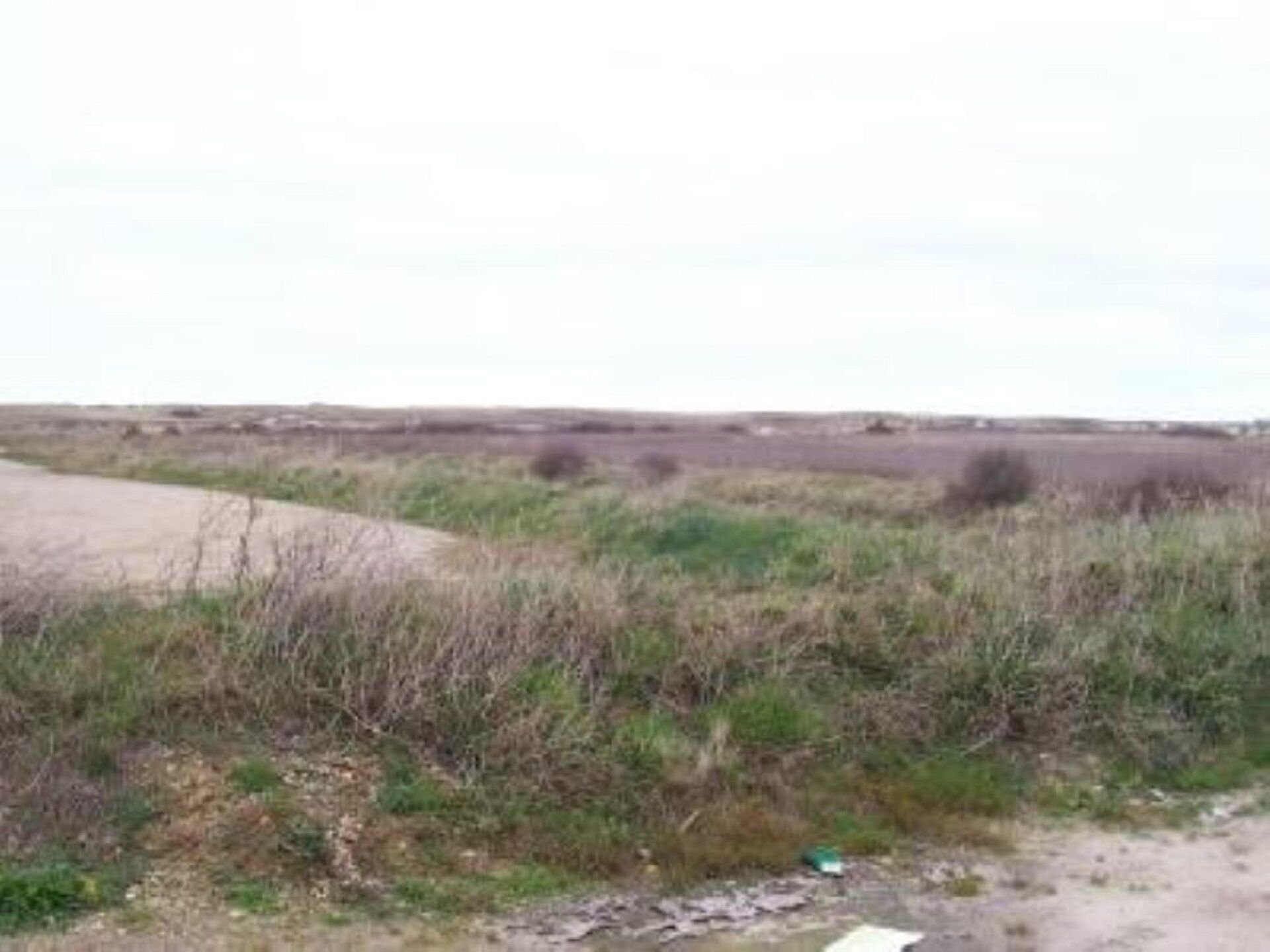A rural landscape with a dirt path, sparse vegetation, and a flat horizon.