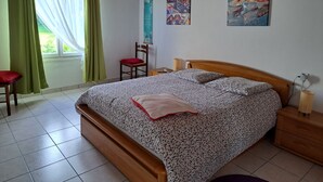A bedroom with a wooden bed, a chair, a bedside table, and a window with curtains.
