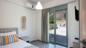 A modern hotel room with a bed, a bedside table, a small stool, and a sliding glass door leading to an outdoor area.
