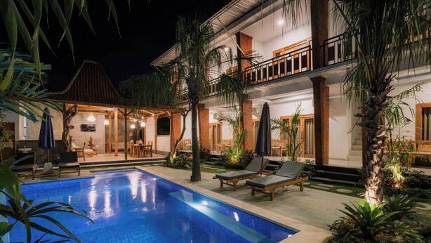 A poolside area with lounge chairs, a covered seating area, and a well-lit building with a balcony. - Mag Canggu Bali (Canggu)