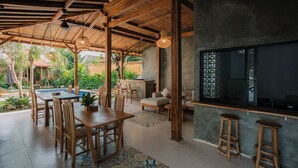 A covered outdoor dining area with wooden furniture, a pool, and a bar area with stools. - Mag Canggu Bali (Canggu)