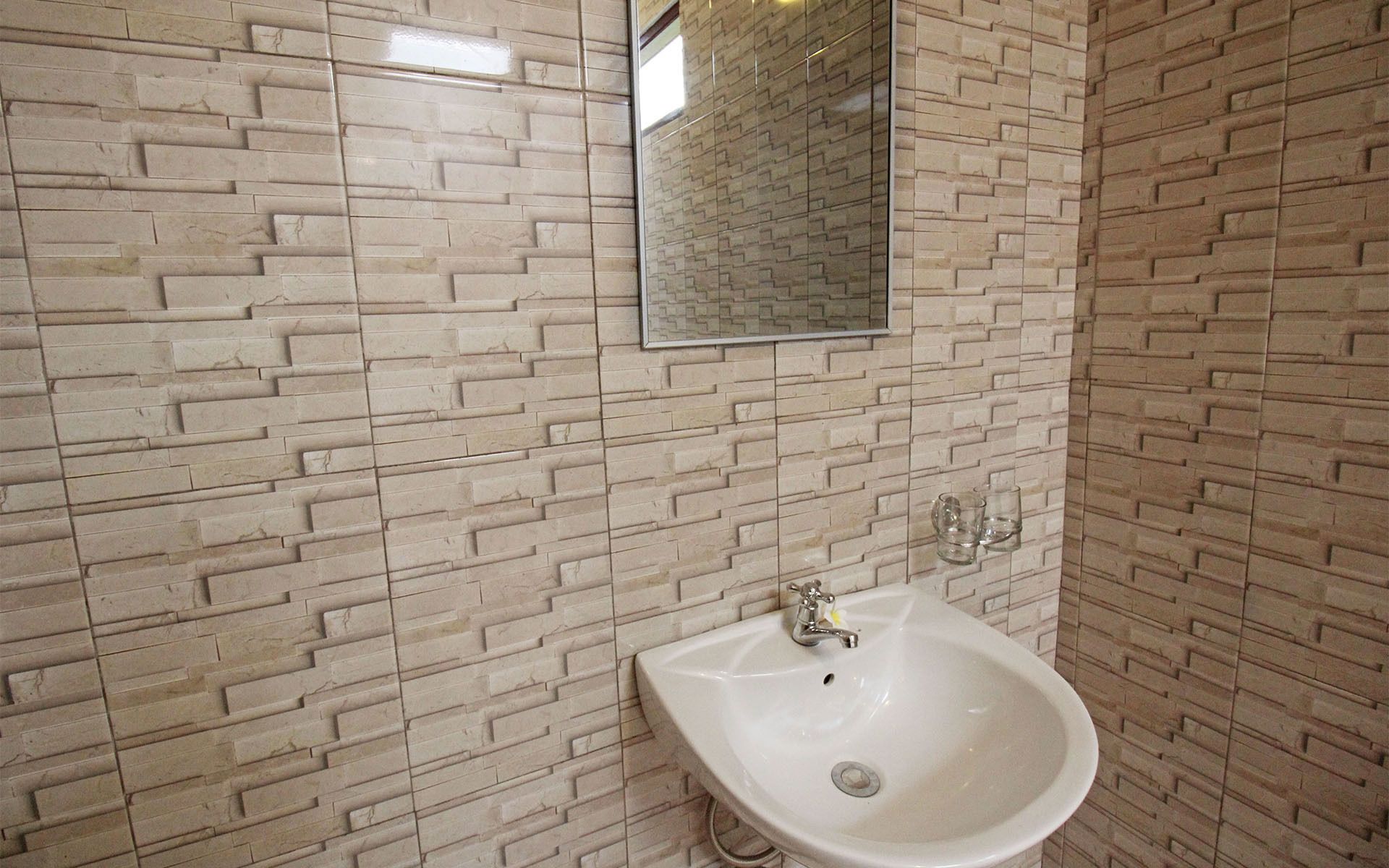 A bathroom with a white sink, a mirror, and a tiled wall with a brick pattern.