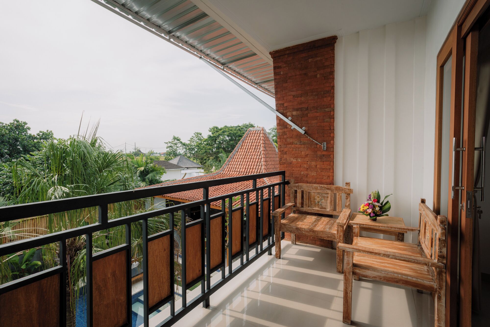 A balcony with a wooden railing, a brick wall, and a view of a house with a tiled roof.