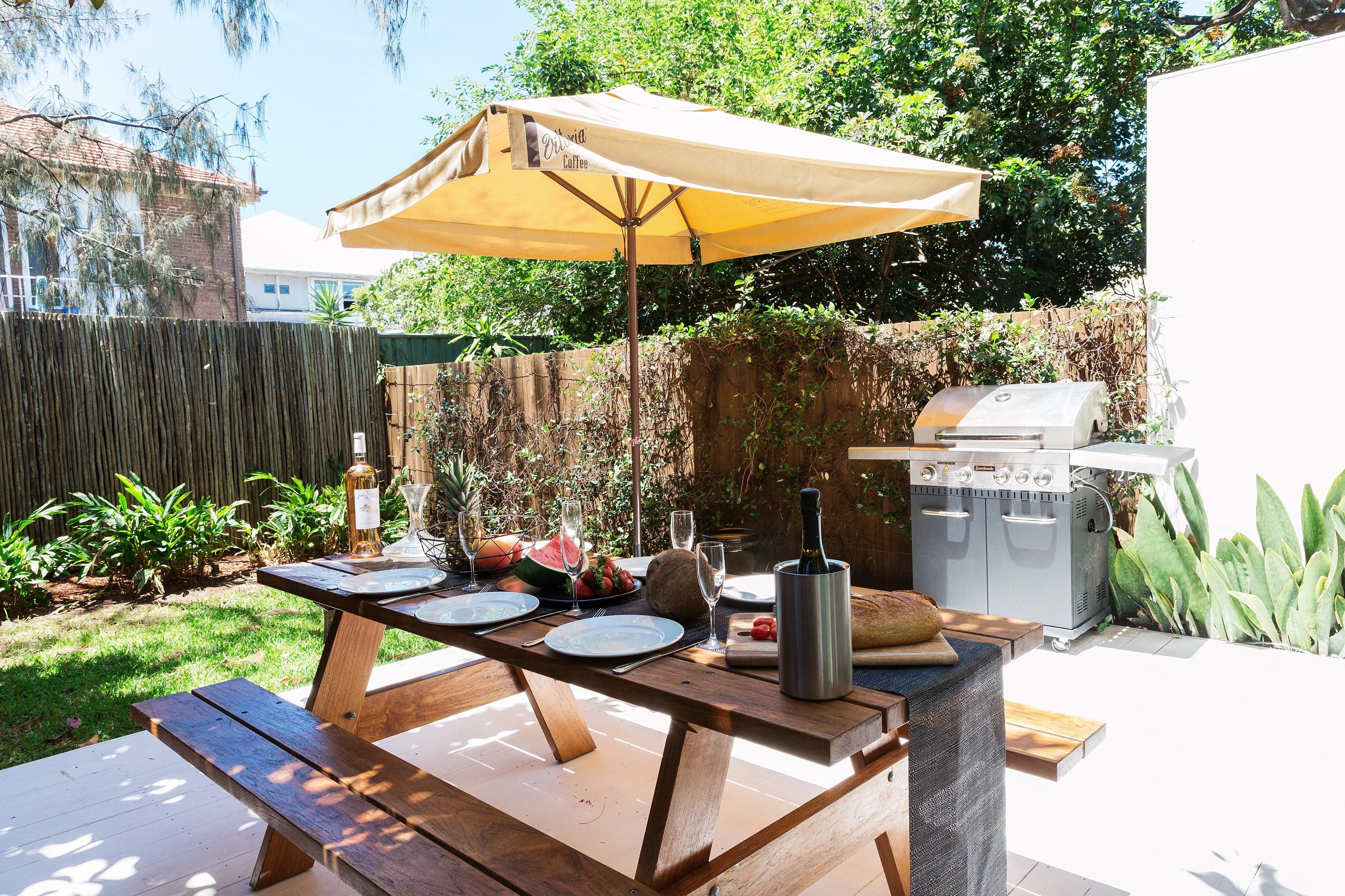 Een buitenmeede met een houten tafel, een gele parasol en een barbecue.