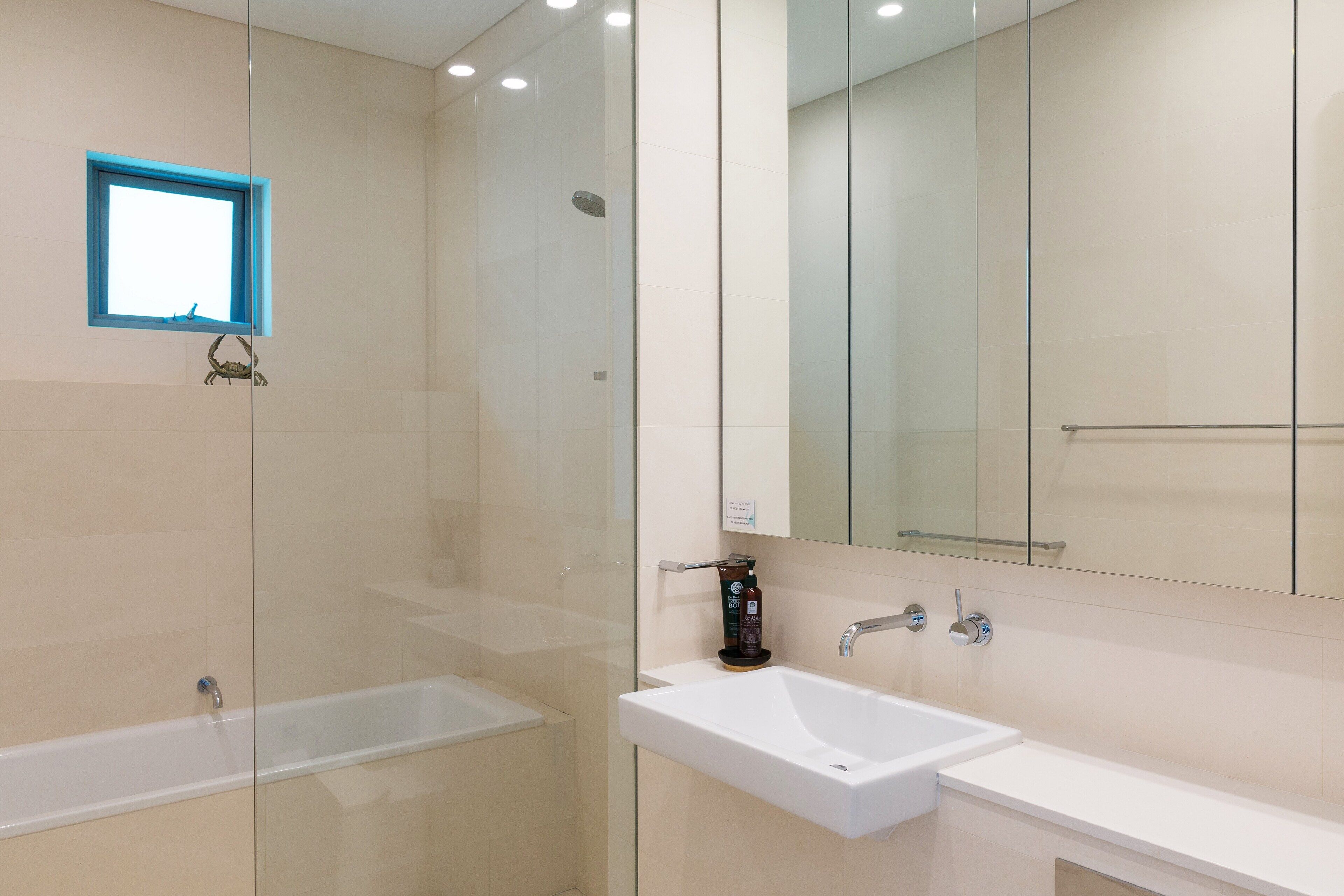 Een moderne badkamer met een douchecabine van glas, een witte wastafel en een grote spiegel.