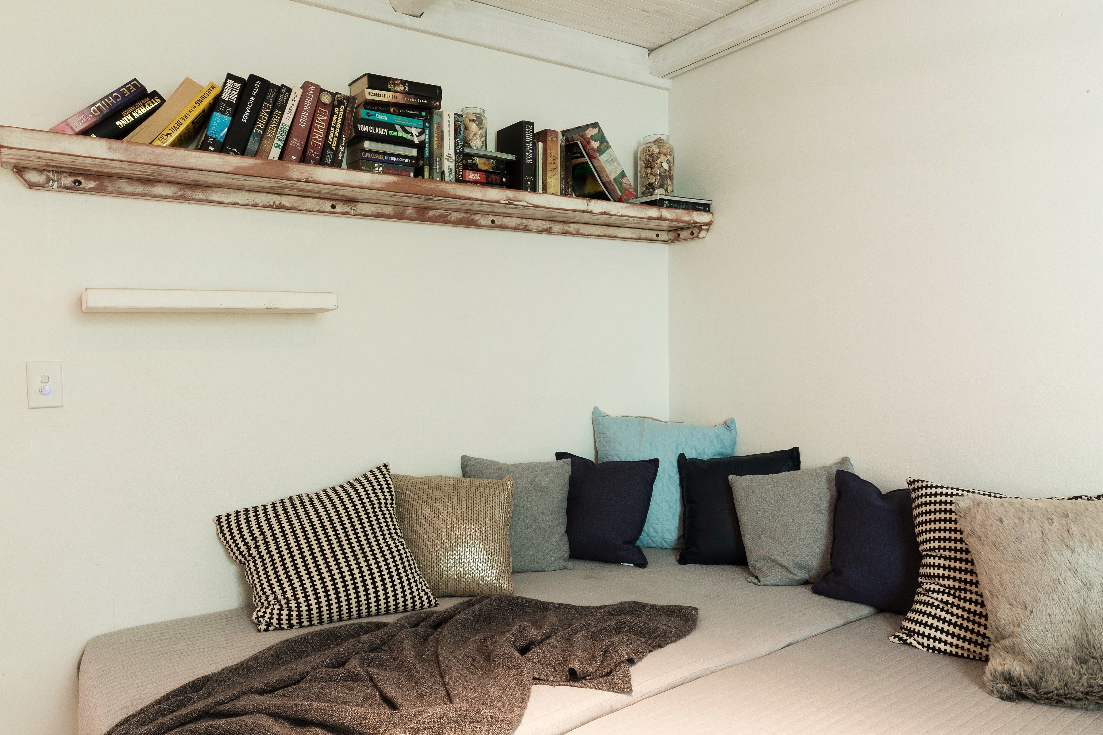 A cozy living room with a sofa, pillows, a blanket, and a bookshelf with books and decorative items.