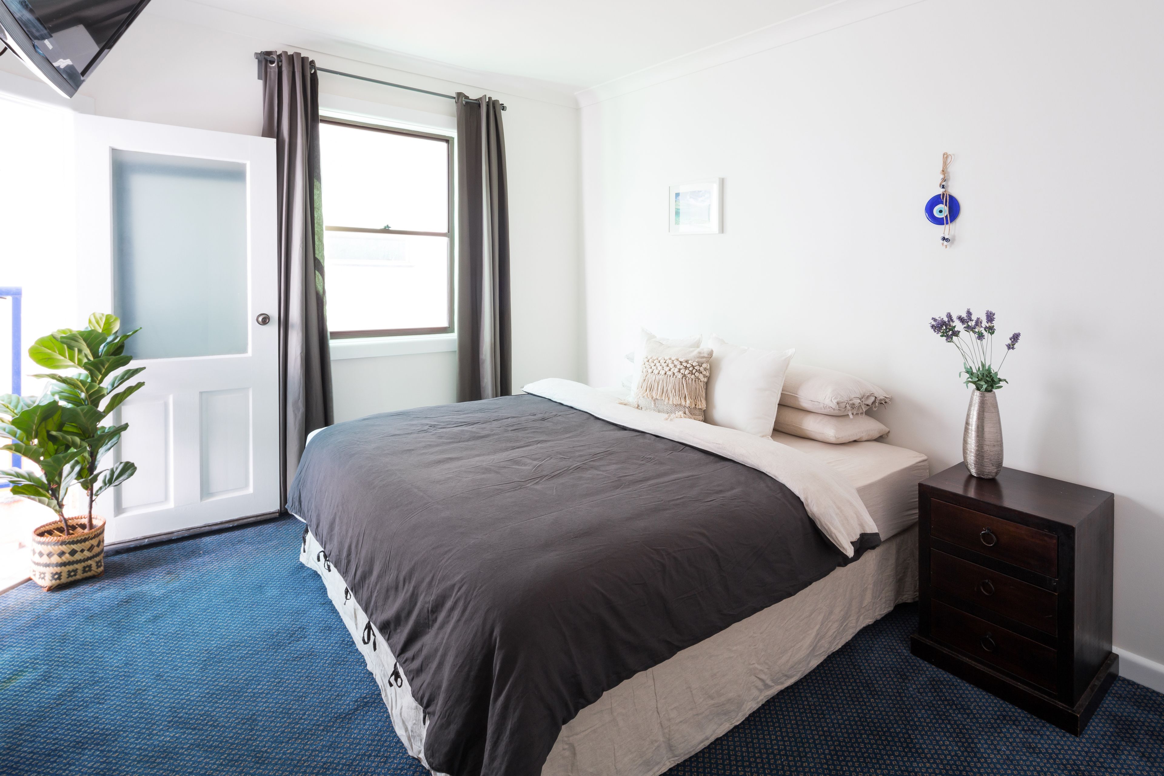 A bedroom with a bed, a nightstand, a potted plant, and a window with curtains.
