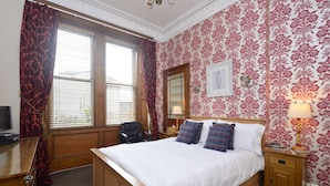 A bedroom with a wooden bed, a desk, a chair, and a window with curtains. - Jo Rooms (Bidhannagar)