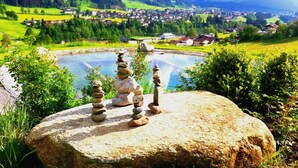 A serene landscape with a pond, a stack of stones, and a village in the distance.