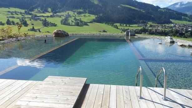 A wooden deck leading to a clear pool with a mountain backdrop.