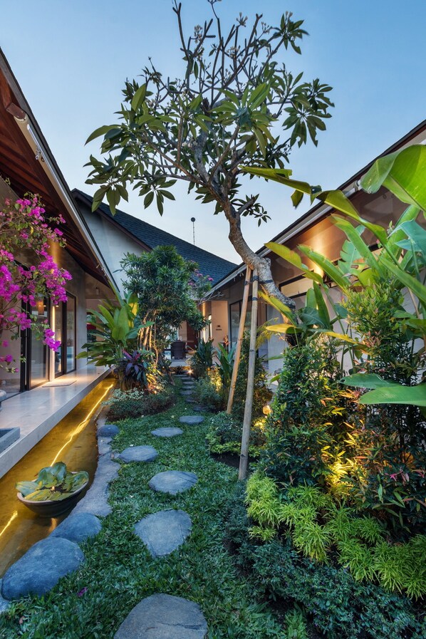 Una casa moderna con jardín que incluye una fuente, piedras para pisar y diversas plantas.