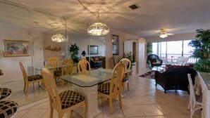 A dining area with a glass table and wooden chairs, a ceiling fan, and a view of the outdoors. - Million Dollar View  Bay Sunrises & Gulf Sunsets-Feb and March open 2025 (Sarasota)