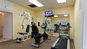 A fitness center with cardio equipment, weight machines, and a television screen displaying a news program. - Million Dollar View  Bay Sunrises & Gulf Sunsets-Feb and March open 2025 (Sarasota)