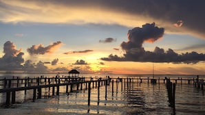 Un muelle se adentra en aguas tranquilas con un atardecer de fondo.