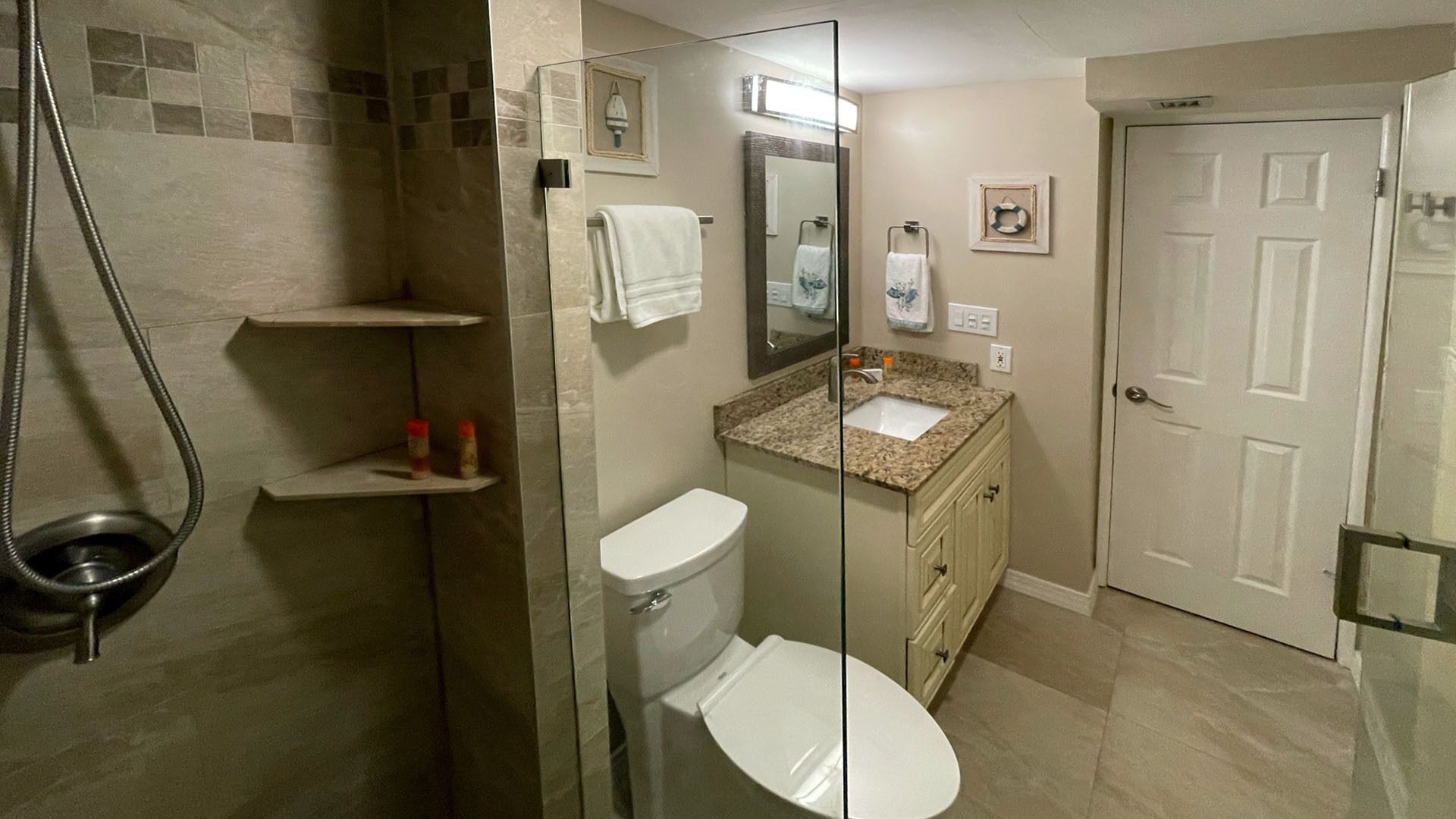 Une salle de bain avec une douche à parois de verre, des toilettes, un lavabo avec un plan de travail en granit et une porte.
