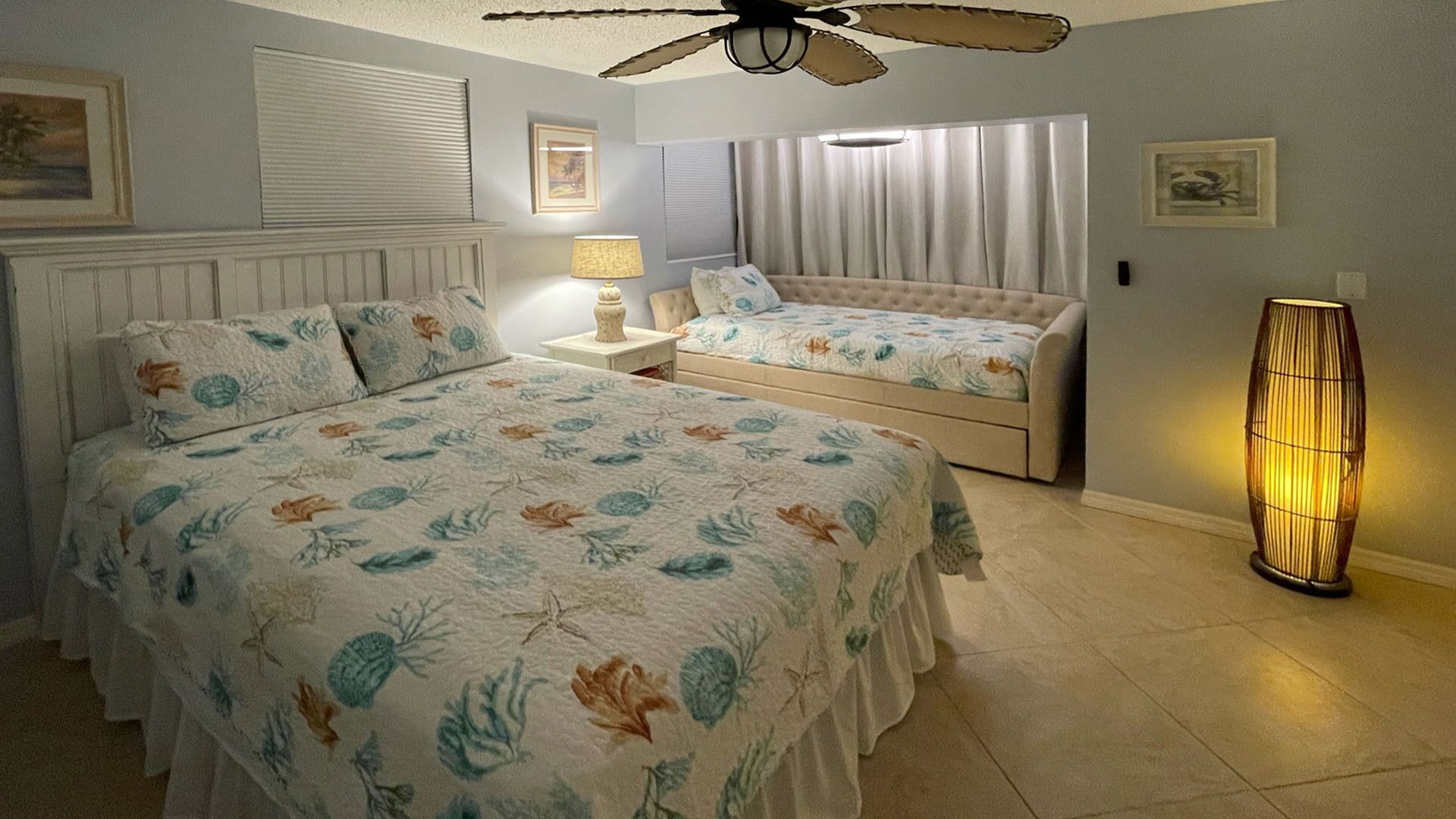 Habitació d'hotel amb dos llits, un ventilador de sostre, una làmpada i una làmpada de peu.