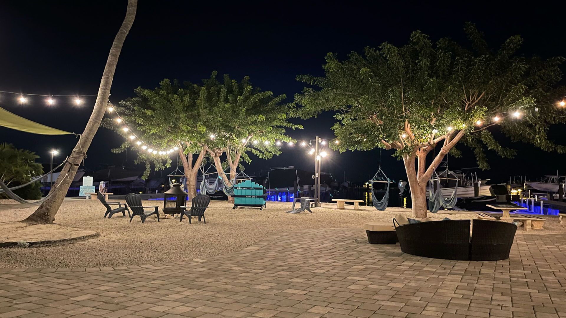 Un espacio al aire libre con sillas y mesas, luces colgantes y árboles.