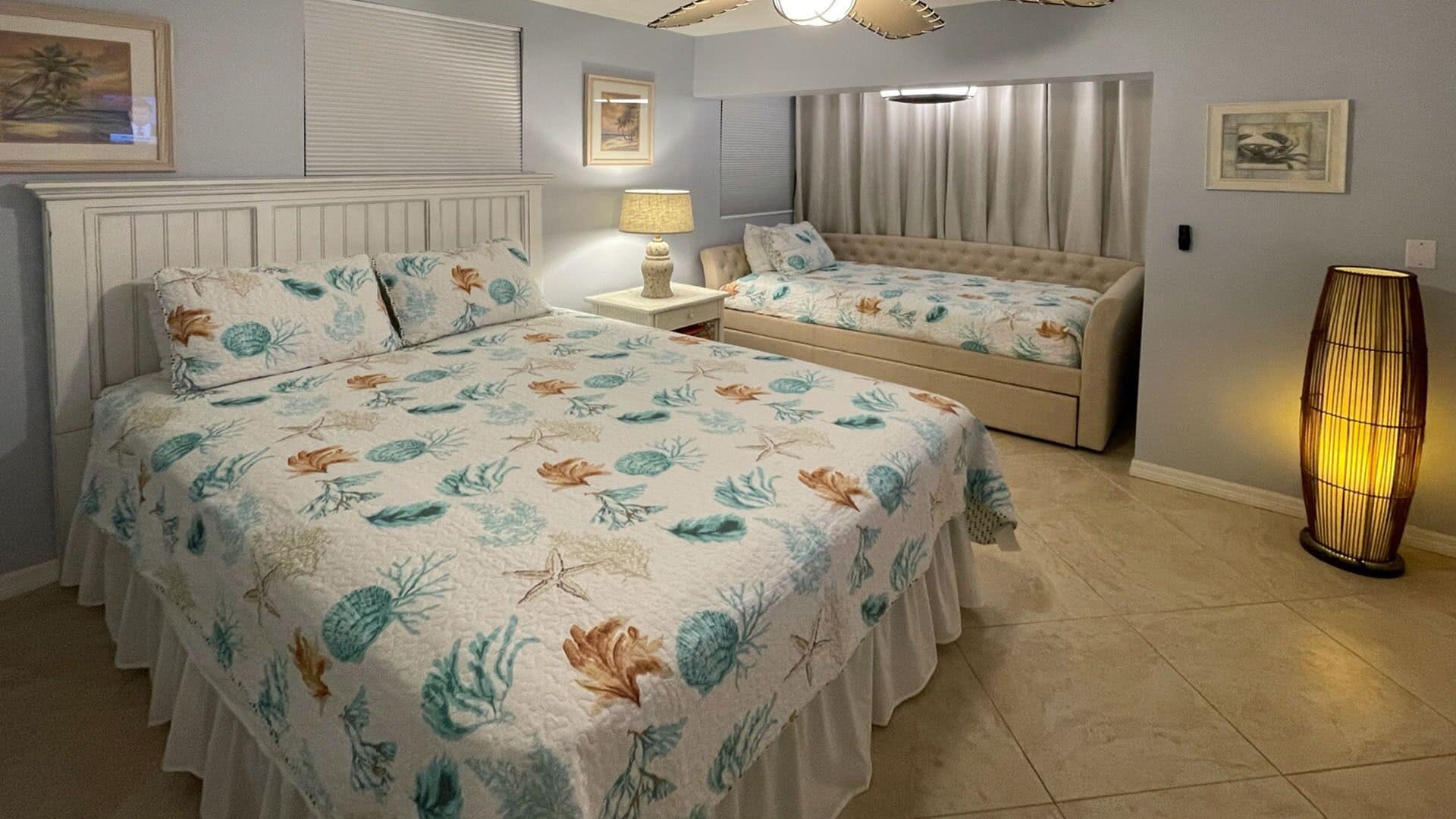 A bedroom with a large bed, a smaller bed, a nightstand, a lamp, and a floor lamp.