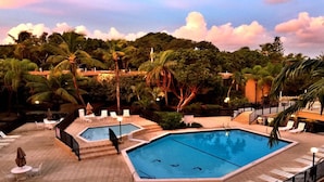 Un área de piscina con dos piscinas, sillas de descanso y palmeras.