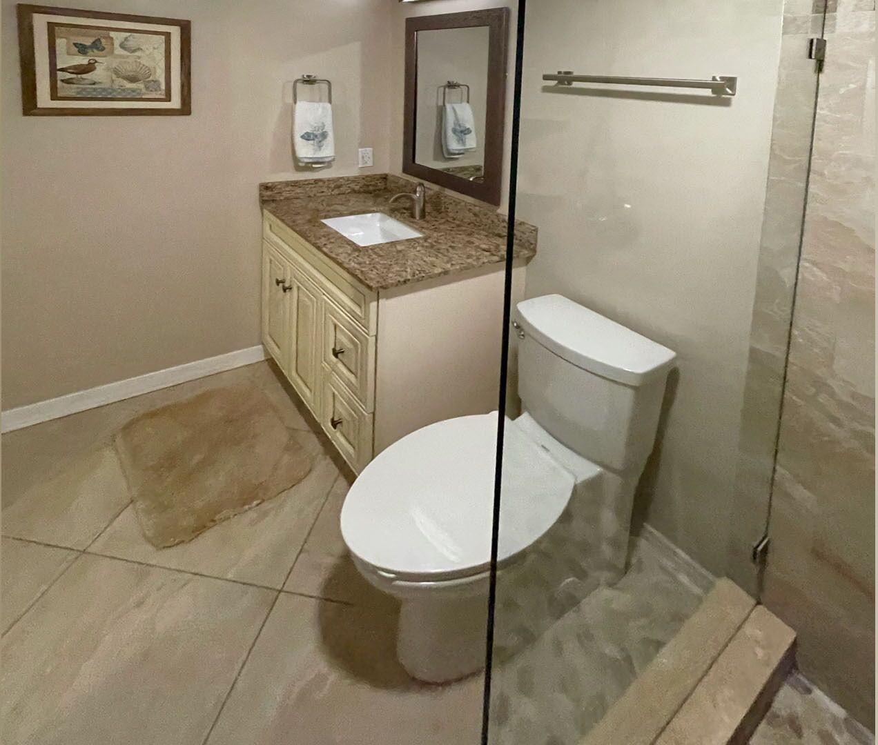 Une salle de bain avec des toilettes blanches, un lavabo doté d’un plan de travail en marbre et une cabine de douche en verre.