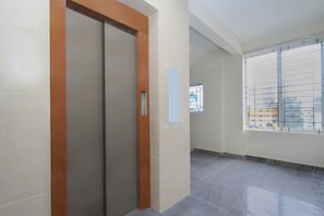Un corridoio con una porta in legno, una finestra con inferriate e un pavimento piastrellato.