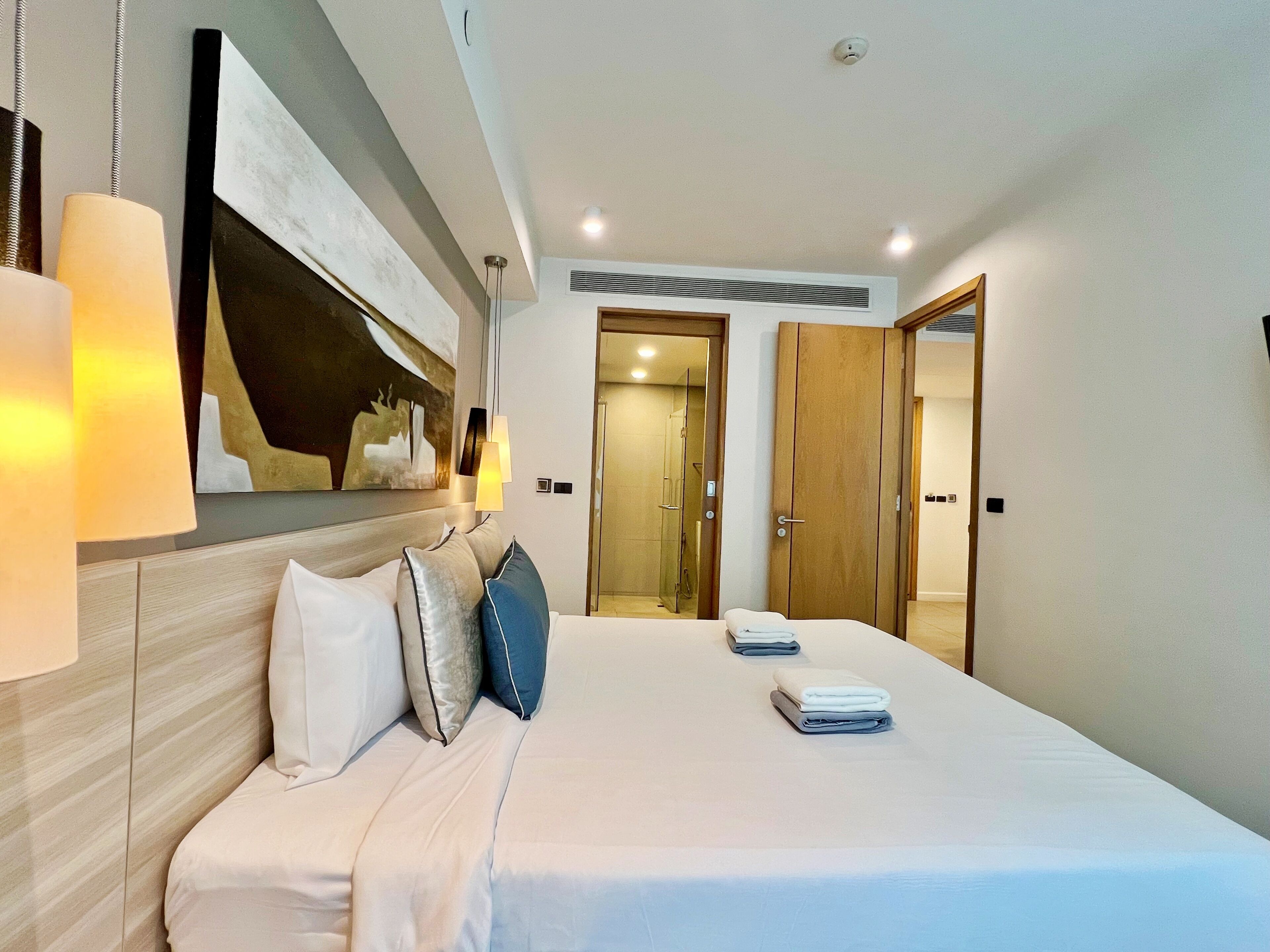 A modern hotel room with a large bed, a headboard with artwork, a mirror, and a wardrobe.