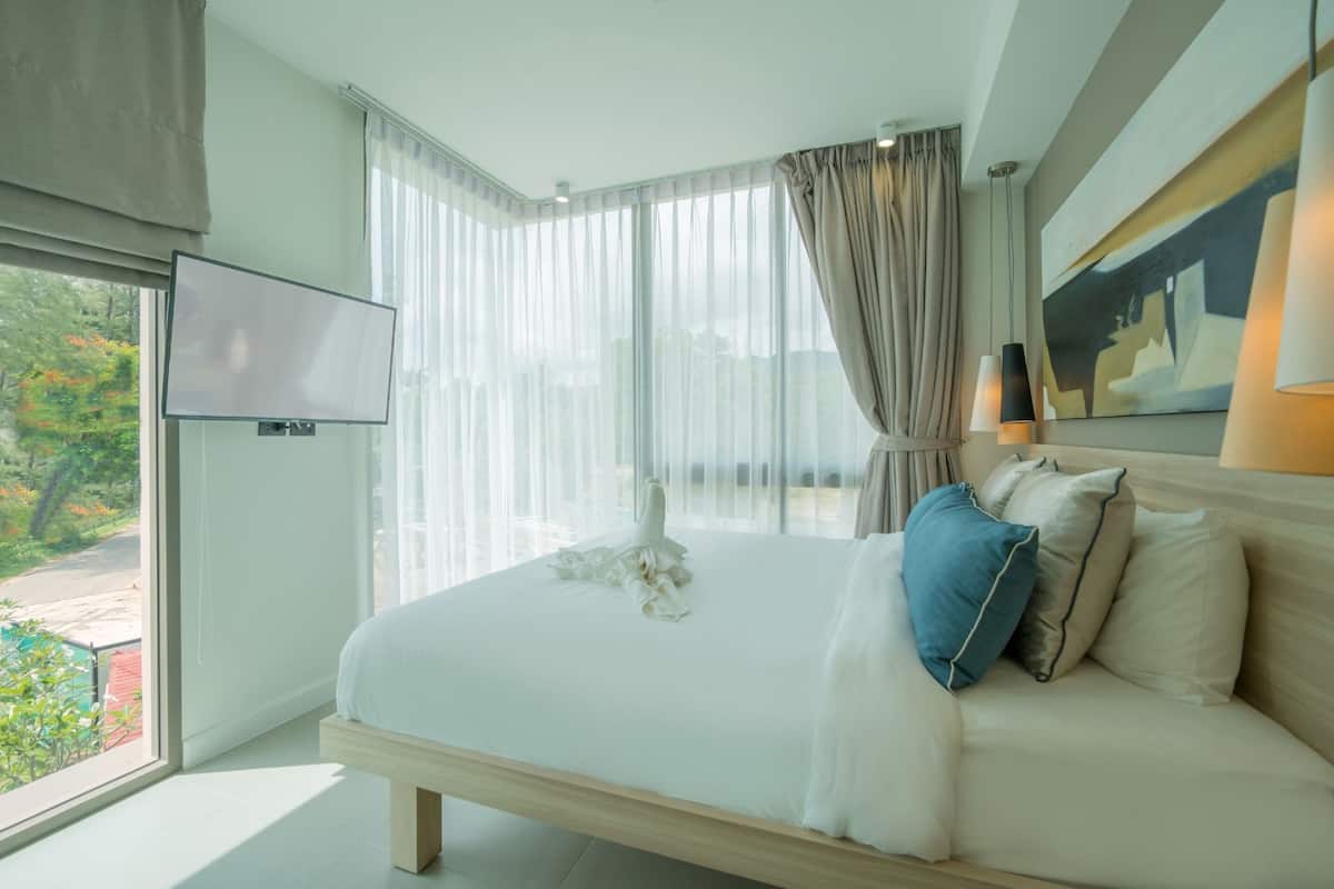 Une chambre d’hôtel moderne dotée d’un grand lit, d’un téléviseur à écran plat, d’une grande fenêtre avec des rideaux légers et d’un tableau au mur.