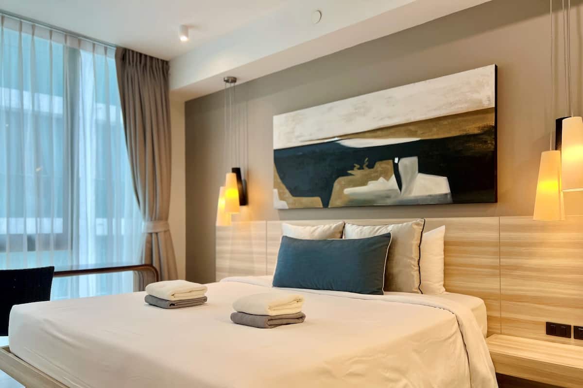 Une chambre d’hôtel moderne avec un grand lit, un tableau au mur et une fenêtre avec des rideaux.