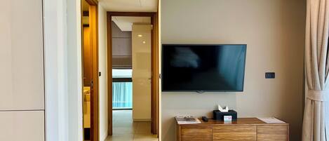 A hotel room with a flat-screen TV mounted on the wall, a wooden cabinet below it, and a door leading to another room.