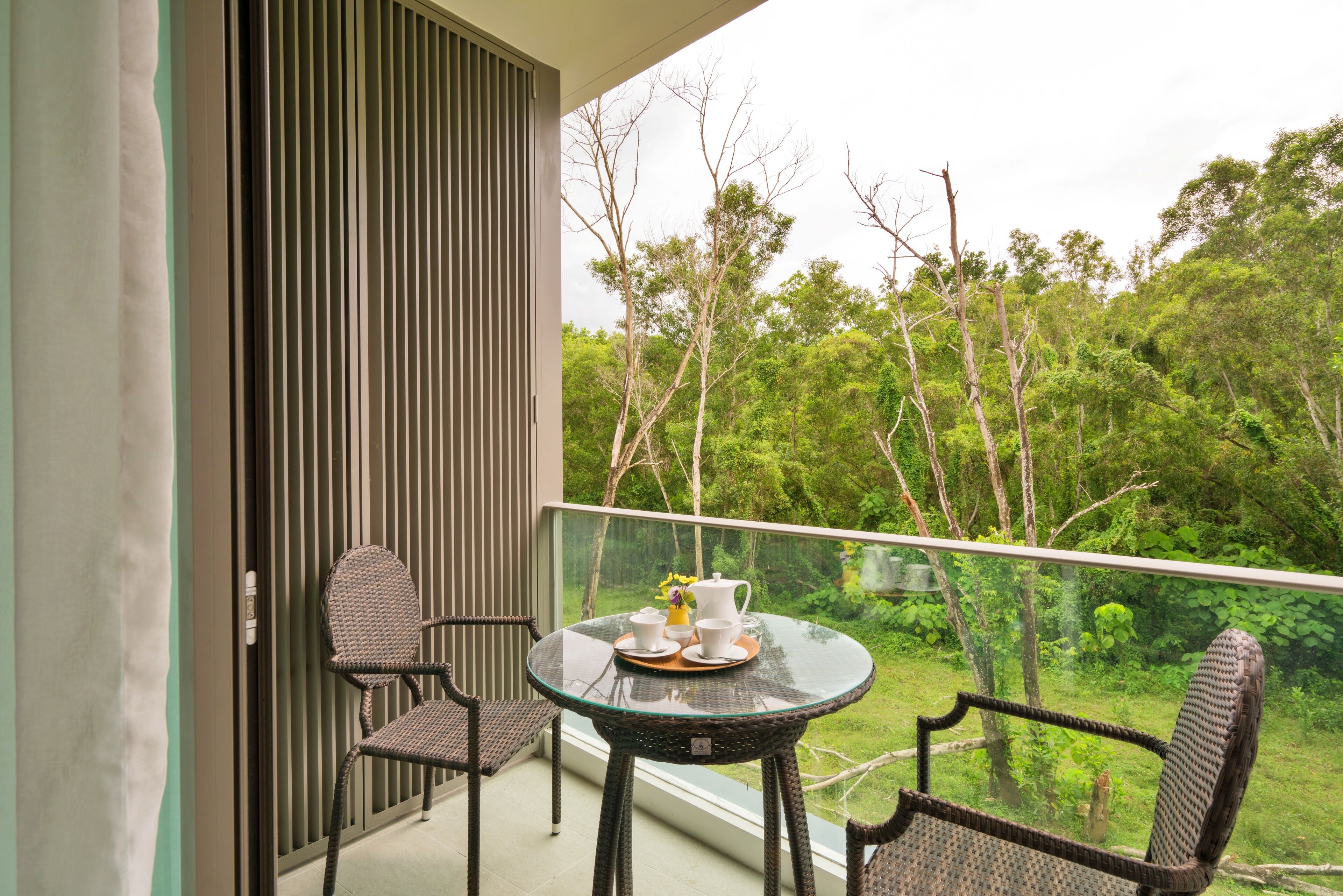 A balcony with a glass table, wicker chairs, and a view of a lush forest.