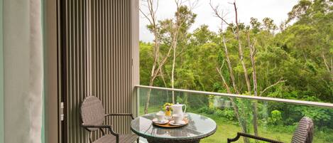 A balcony with a glass table, wicker chairs, and a view of a lush forest.