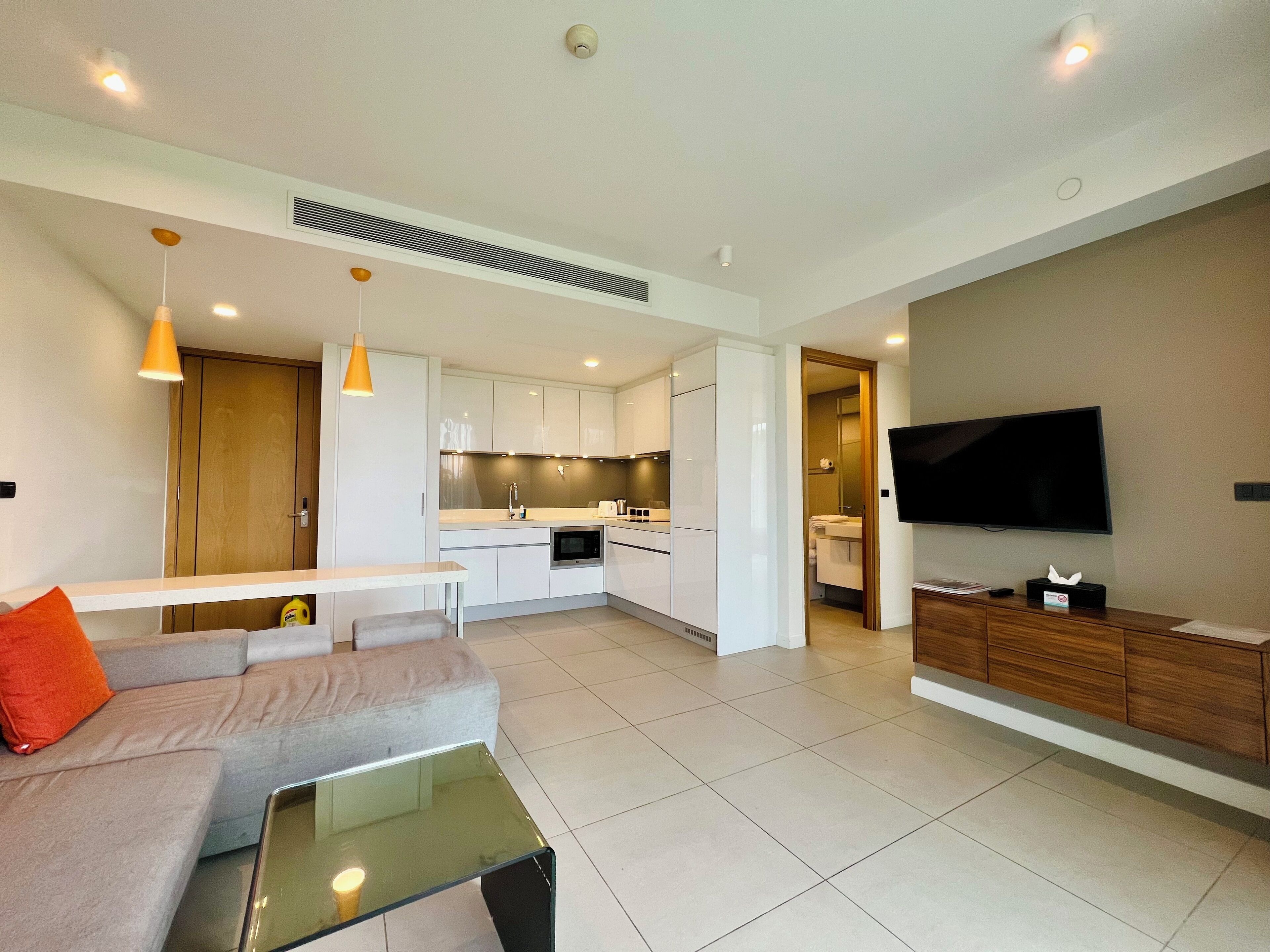 A modern living room with a sofa, a glass coffee table, and a TV mounted on the wall.