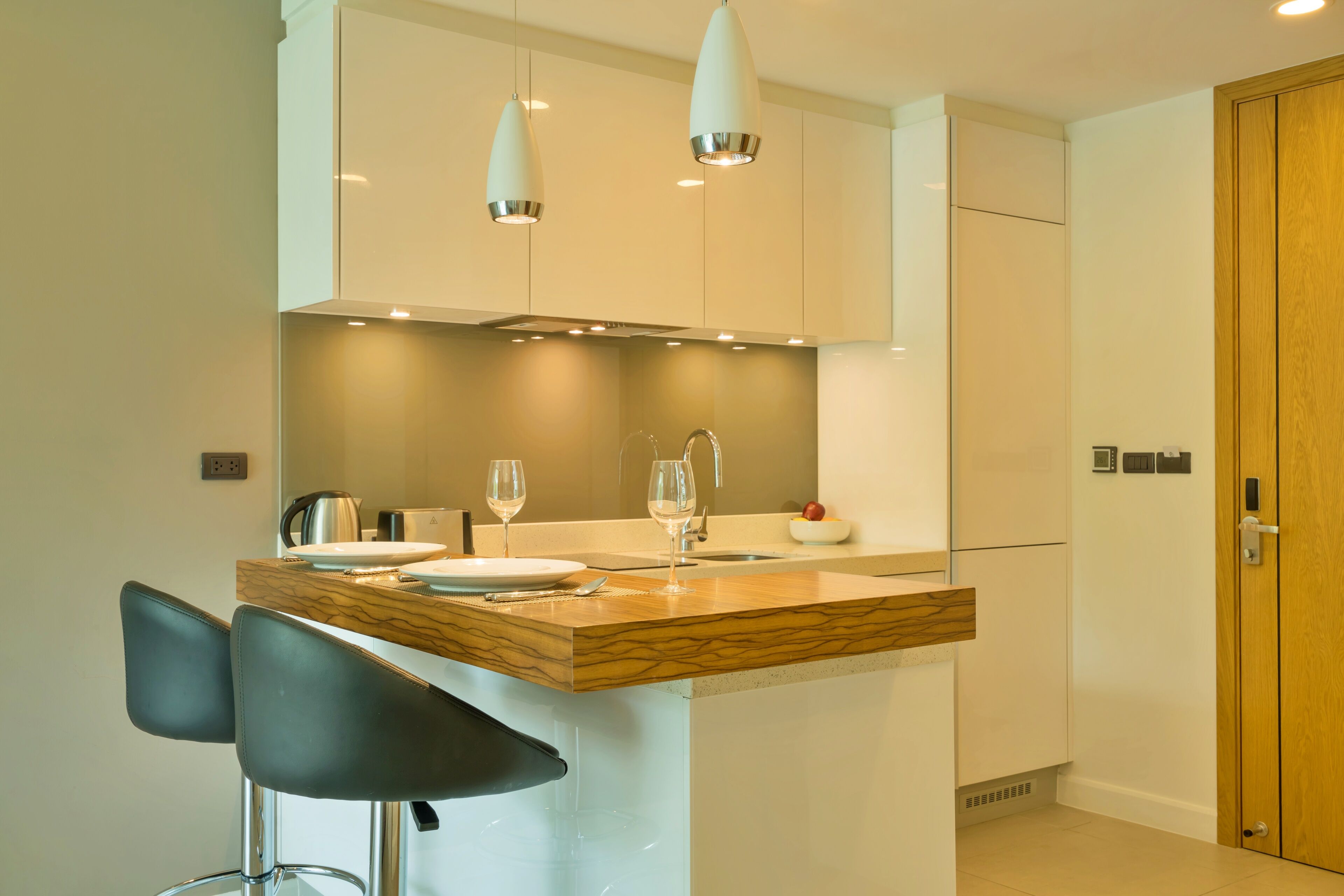 A modern kitchen with a marble countertop, two bar stools, pendant lights, and a wooden door.