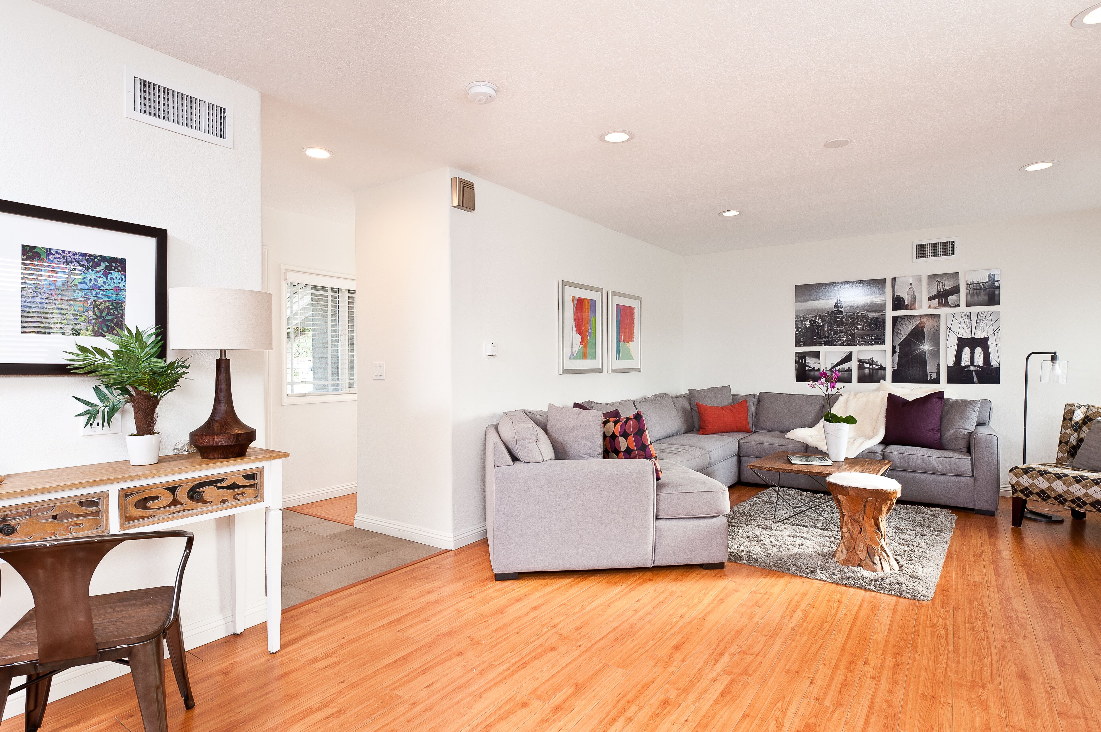A modern living room with a grey sectional sofa, a wooden coffee table, and a dining area with a white table and dark chairs.