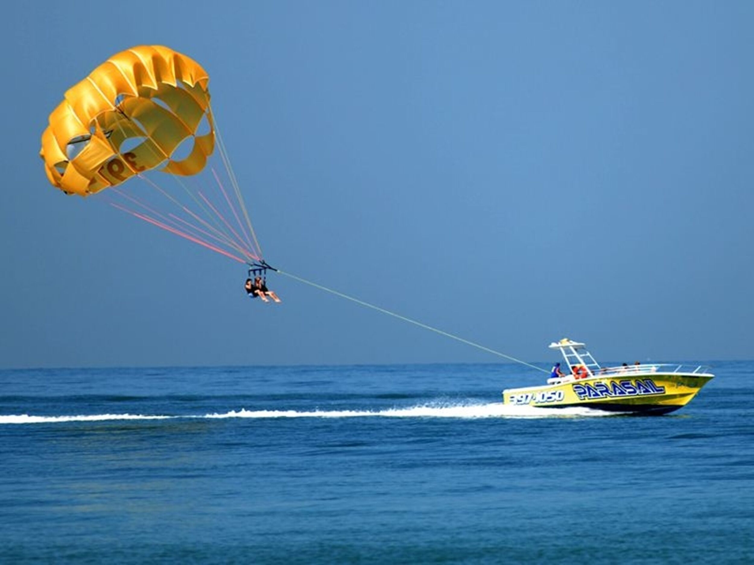 A parasailing activity with a yellow boat and a parachute in the background.