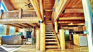 A wooden interior with a staircase leading to a loft area, a kitchen with wooden cabinets, and a stone fireplace. - Family Favorite! no curves, pets , theater, , yard , fire pit , min to strip  (SEVIERVILLE)