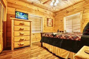 Een slaapkamer in een houten chalet, met een bed, een dressoir en een televisie aan de muur.