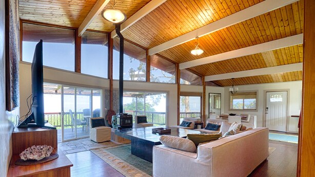 A spacious living area with a high ceiling and large windows, a fireplace, and a television. - Hale Waiaha Spacious Holualoa Home  (Holualoa)