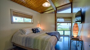 A bedroom with a bed, bedside lamps, a television, and a window with a view. - Hale Waiaha Spacious Holualoa Home  (Holualoa)