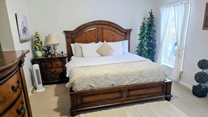 Een slaapkamer met een houten bed, een nachtkastje, een dressoir, een radiator, een kerstboom en een raam met gordijnen.
