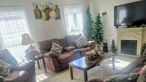 Een woonkamer met een bank, fauteuils, een salontafel, een openhaard en een televisietoestel.