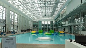 Ein Hallenbad mit Glasdach, klarem Wasser und Schwimmspielzeug.