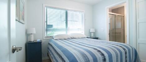 Une chambre à coucher avec un lit, une fenêtre, une porte et une table de chevet avec une lampe.